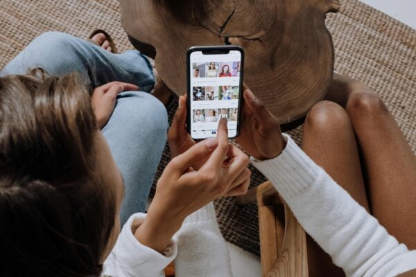 Two people looking at social media on a smartphone at a wooden table.